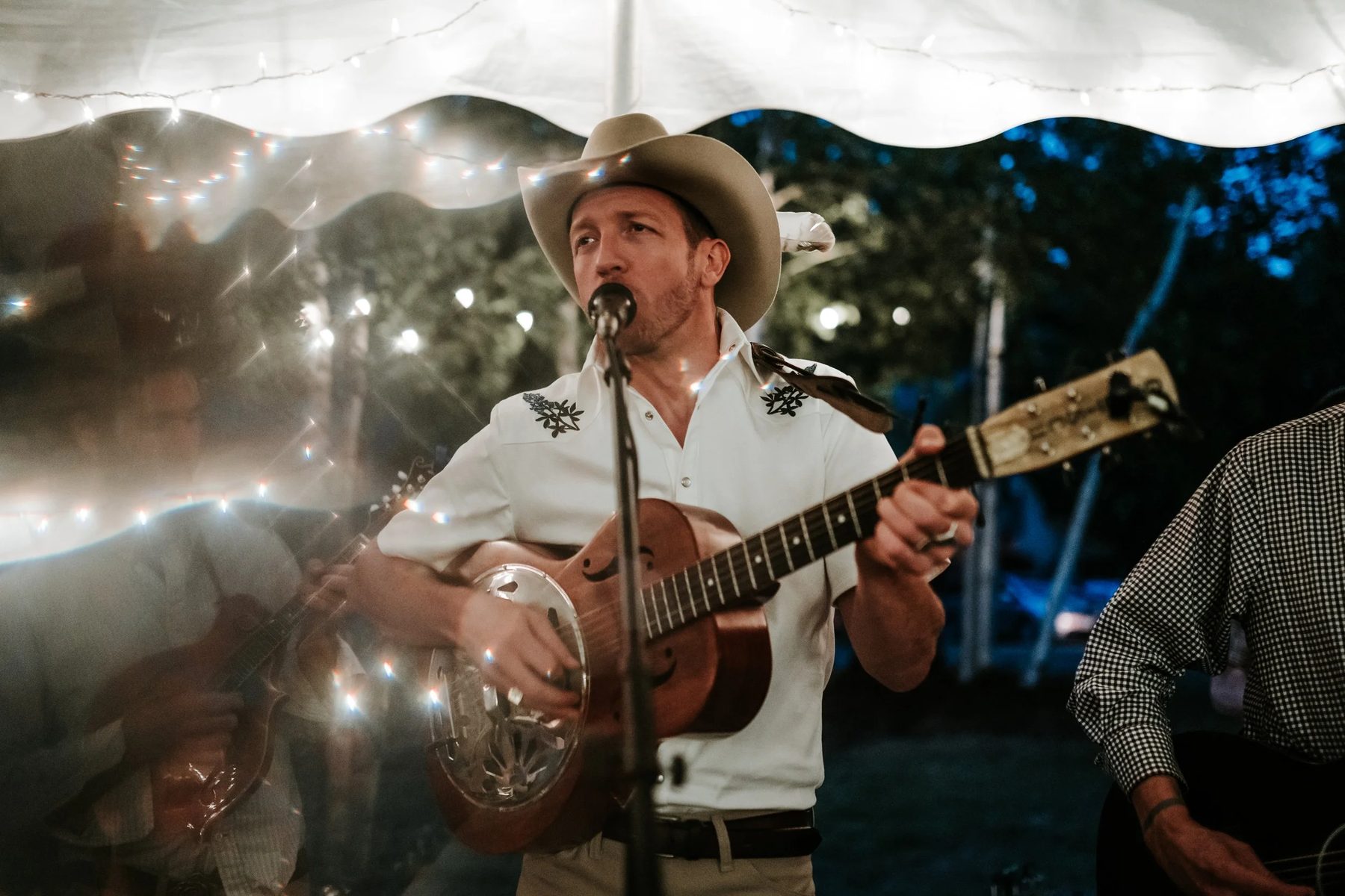 Patrick B Ray singing into a microphone under a lit tent