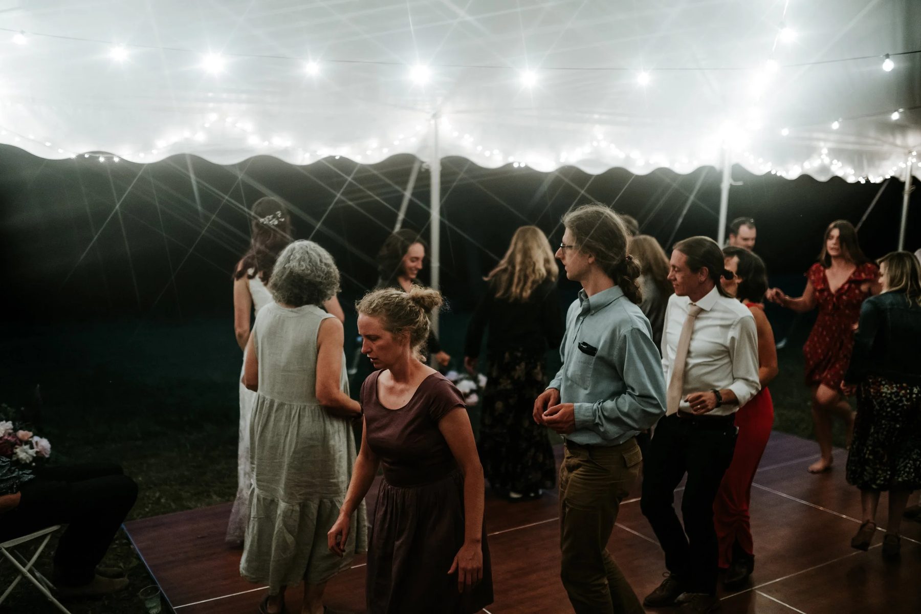 Guests dancing under a tent strung with lights at dusk